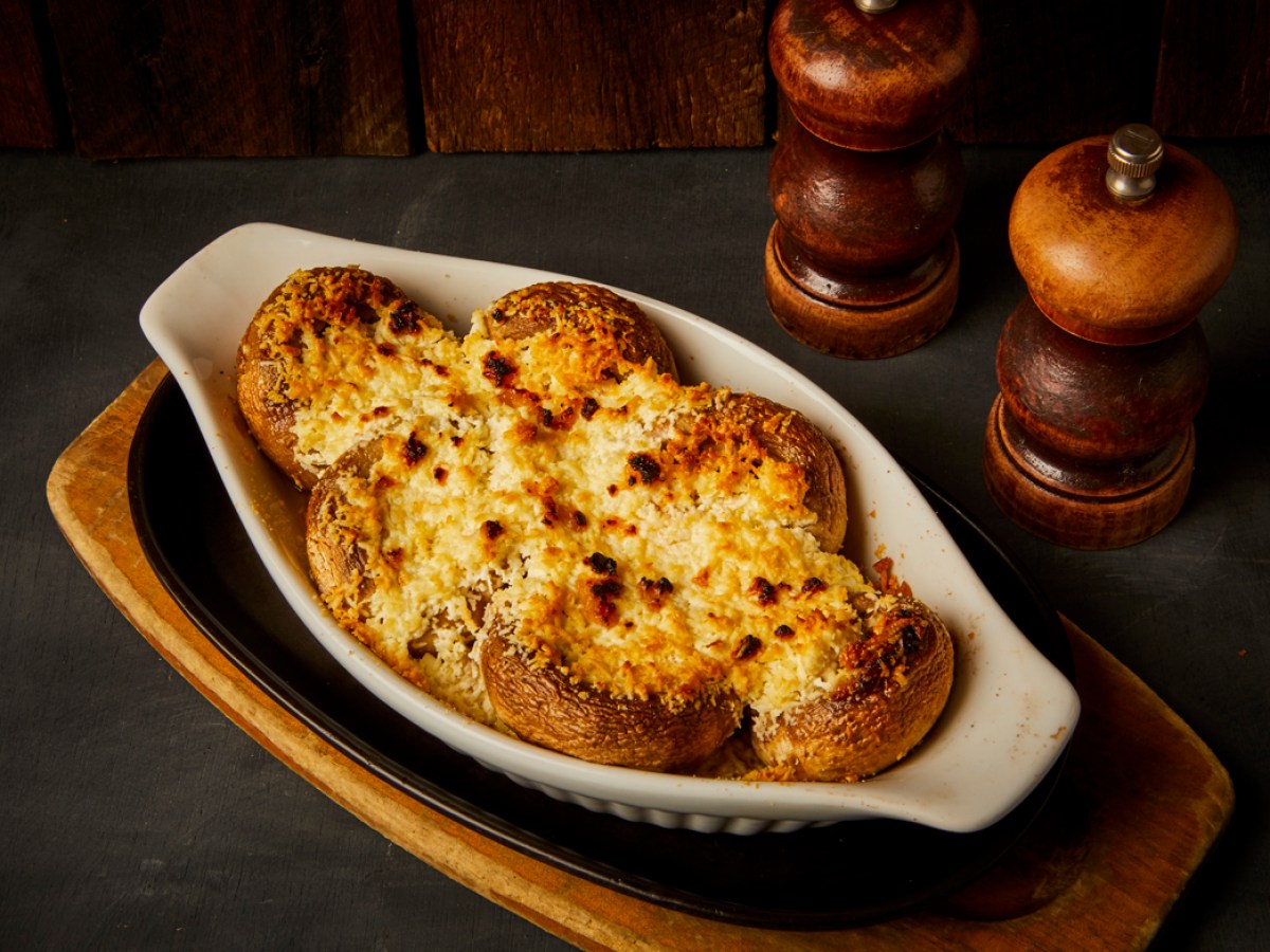 Baked mushrooms topped with cheese in a white dish, with two pepper mills nearby.