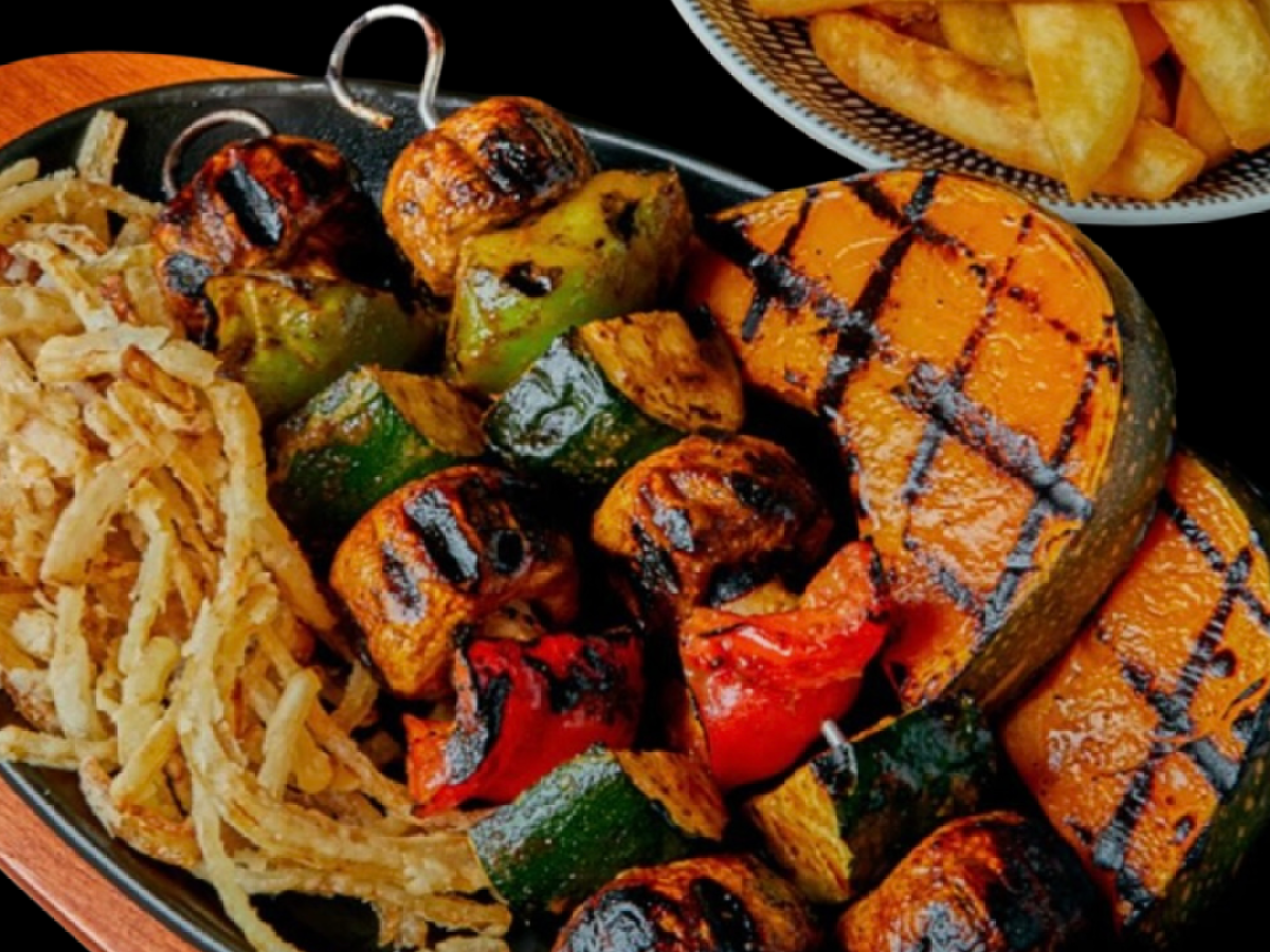 Grilled vegetable skewers with sliced pumpkin and fried onion rings on a black platter; fries in a bowl.