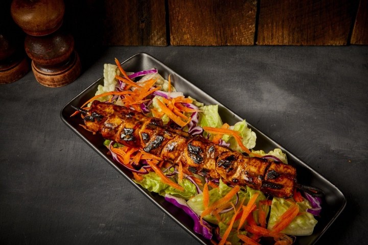 Grilled kebab skewer on salad with lettuce and shredded carrots.