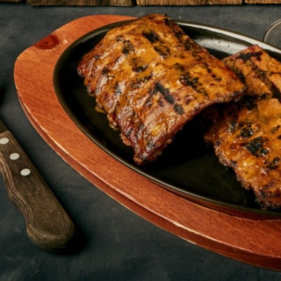 Grilled ribs on a platter with cutlery on the side.